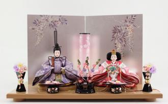 銀箔紙に藤の「金彩加工」を施したお屏風は淡い色味の親王様のお衣装を上品に演出しています。お菓子のお道具やつまみ細工のお花がこだわりの溢れたお雛様です。
