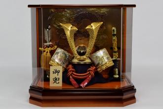 彫金の吹返しが特長の金兜。家具調塗の六角アクリルケースで比較的軽量でお手軽な兜ケース飾りです。コンパクトながらお手軽です。