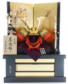 上質な正絹素材を用いて堂々とした風格のある兜に仕上げました。
金の屏風には大きな龍を配しています。
贅沢な駿河塗の飾り台は、飾る場所のインテリアを選ばないデザインです。また、飾り台が収納箱になっており、屏風以外を格納できるので大変便利です。