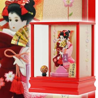 こちらの羽子板付き「聖美(赤)8号 正絹しぼり羽子板付」(カブセケース入り)は、正絹しぼり仕立てと、ベルベット地に桜柄刺繍がほどこされたお袖の、代表的なスタイルの柄の一つである「道成寺」です。
能の演目の一幕を模した舞い姿の優美な印象で、「将来幸せになれますように・・・」という意味合いがあるものです。
また、まり飾りは女の子の初正月を祝う羽子板に添えられる事の多いお飾りですが、ただ華やかさを増すためだけでなく、「丸く健やかに美しく育つように」との願いが込められています。
ケースのバックには、桜柄の刺繍がデザインされて、春らしいケース飾りです。
お子様の幸せを願うご両親の想いが込められた、女の子のお守りとして受け継がれてきた日本の伝統的縁起物です。